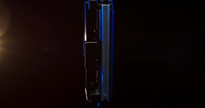 Close up of a vertical industrial linear actuator with blue light accent in a dark setting