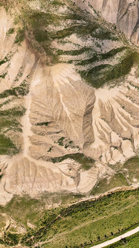 Aerial view of the rugged, earthy landscape is etched with deep ravines and sparse vegetation, a tapestry of beige and green textures, Centuripe, Sicilia, Italy.