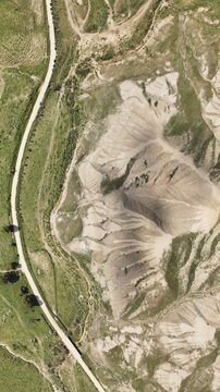 Aerial view of sun-scorched earth sculpted by wind and time, bisected by a pale ribbon of road winding through the arid landscape, Centuripe, Sicilia, Italy.