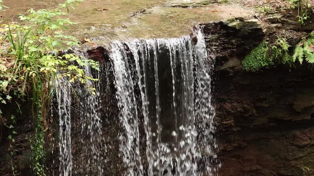 Small waterfall flowing over rock edge in forest with natural stream water