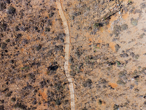 Aerial view of a winding path cutting through the arid landscape, a ribbon of light amidst the ochre and umber tones, Rhiy di-Hoq, Socotra, Yemen.
