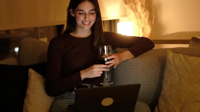 Young Woman Laughing on Video Call with Laptop While Enjoying Red Wine at Home