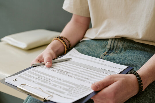 Young adult patient holding medical intake form and pen while waiting for consultation, showing healthcare registration process. Useful for clinic marketing, insurance, patient onboarding