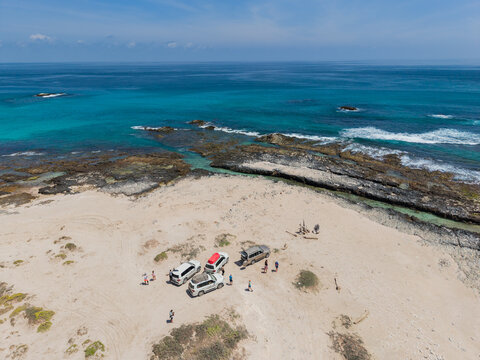 Aerial view of cars parked on the sandy beach meeting the turquoise ocean, a stark contrast of arid land and vibrant sea, Erissel, Socotra, Yemen.