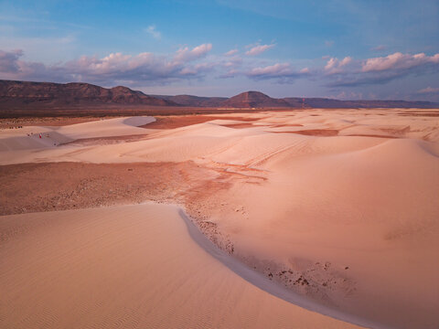 Aerial view of undulating dunes of white sand meet reddish plains under a vast blue sky, revealing the stark beauty of the landscape, Hamlah, Socotra, Yemen.