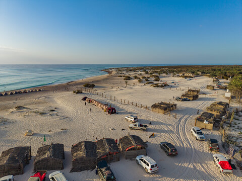Aerial view of the contrasting thatched huts and parked cars dotting the sandy beach against the backdrop of the turquoise sea, Kadrihnitin, Socotra, Yemen.