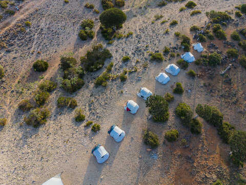 Aerial view of a neat row of white tents contrasting against the arid, rocky landscape dotted with sparse greenery, Firmihin, Socotra, Yemen.
