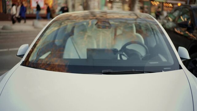 Front view of a modern white electric car parked on a city street with reflections on the windshield
