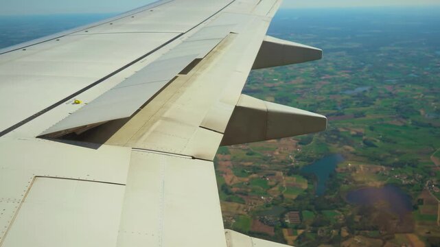 Plane descending over green rural landscape, ailerons working. Jet approaching ground above countryside fields, flaps operating. Aircraft lowering altitude across agricultural terrain, control