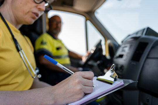 Paramedic writing medical report inside ambulance with driver