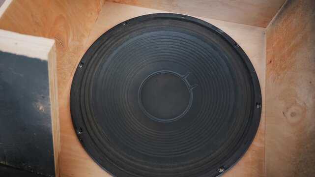 A close-up view of a black paper subwoofer cone mounted inside a wooden acoustic box. Concept of heavy bass vibration, low frequency sound waves, and powerful audio reproduction.