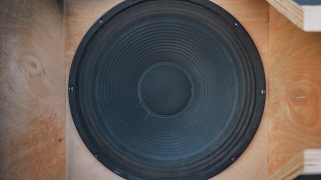 Large black paper speaker cone vibrates rapidly inside a raw wooden acoustic box. Depicts the concept of powerful bass and sound wave generation in acoustic systems.