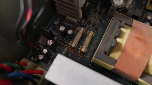 Close up view of an internal computer power supply circuit board featuring glass fuses, electrolytic capacitors, and a metal heat sink. This illustrates an electronic engineering concept.