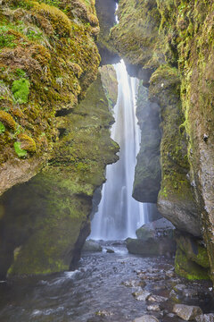 Hidden waterfall falling through a narrow mossy cleft into a rocky pool