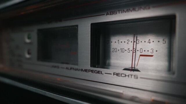 Close-up detail of an analog VU meter on a vintage stereo receiver brushed metal faceplate. German text indicates tuning and recording level. This concept represents retro audio technology.