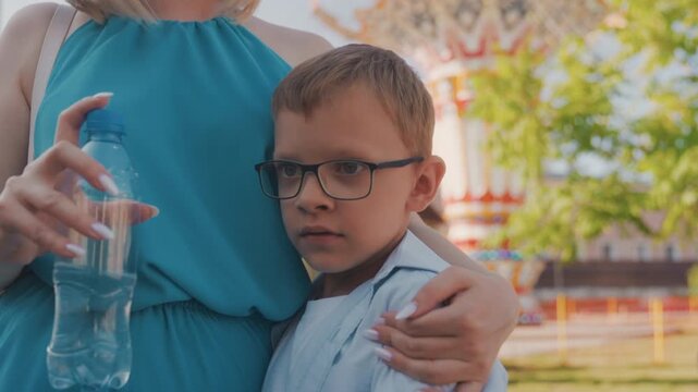 Mother calming boy. Caring mother tenderly comforts her lively boy outdoors with hugs. Mother affectionately embraces and calms her energetic young son during outdoor playtime using gentle hugs