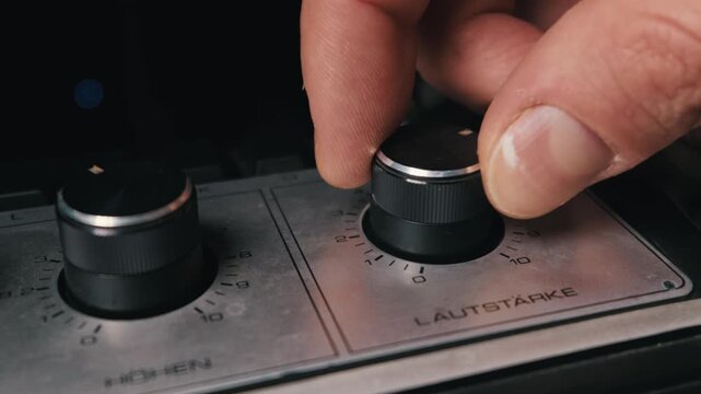 Blurred fingers reach to turn the Lautst rke volume dial on a metallic analog audio amplifier. The tactile adjustment of vintage electronics represents an authentic audio control concept.