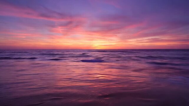 Beautiful orange sunset over the calm sea with soft waves and purple clouds in the sky