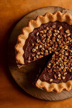 Tarta de chocolate r&uacute;stica con borde de masa ondulada y cobertura de avellanas picadas sobre tabla de madera