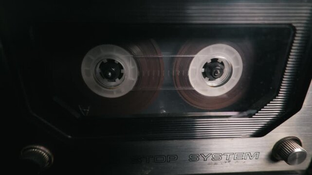 A vintage audio cassette tape spins steadily inside a retro stereo player. Macro focus highlights the magnetic ribbon and white plastic hubs in crisp detail. Brushed metal adds analog charm.