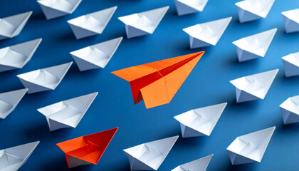 Obraz premium Orange paper plane flying over white origami boats, leadership and disruption concept in business strategy.