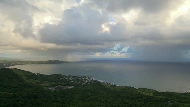 Cinematic drone shot of a lush tropical coastline in Puerto Rico. High angle view of green hills and ocean under a dramatic cloudy and misty sky at dusk.