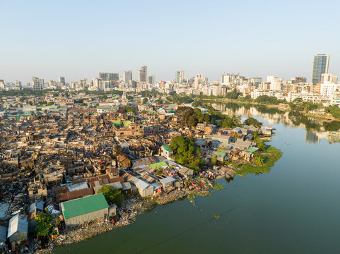 Aerial view of a sharp contrast between the dense, haphazard settlements along the riverbank and the modern skyline in the distance, Dhaka, Dhaka Division, Bangladesh.