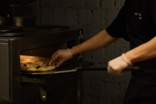 A baker is pulling a tray of warm bread from the oven in a bakery. The setting is lively with the smell of baked goods filling the air. The baker works quickly as customers wait.