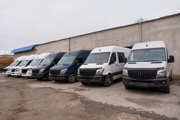 Row of white and dark blue commercial delivery vans parked in a lot against a concrete wall on a cloudy day. © Galka3250
