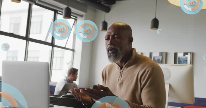 Animation of multiple bar graph icons over african american man having videocall on laptop at office