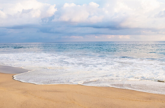 Cumulus clouds over ocean waves on empty beach