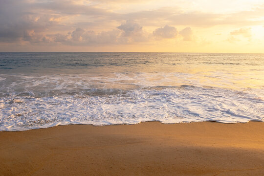 Clouds over ocean waves on empty beach at sunset
