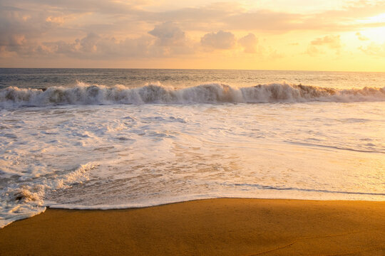 Clouds over ocean waves on empty beach at sunset