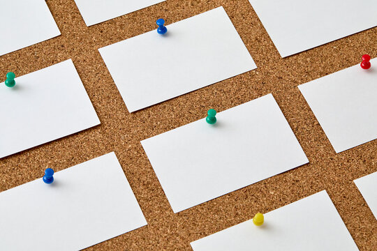 Blank pieces of paper attached to cork board with colorful push pins