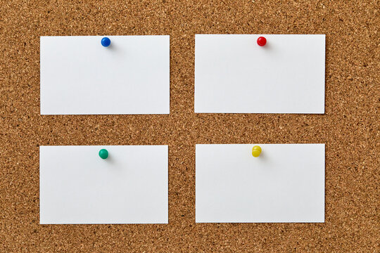 Blank pieces of paper attached to cork board with colorful push pins