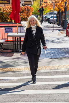 Smiling senior blond businesswoman crossing downtown street