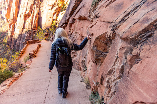Rear view of female hiker touching sandstone cliff on trail to Angels Landing