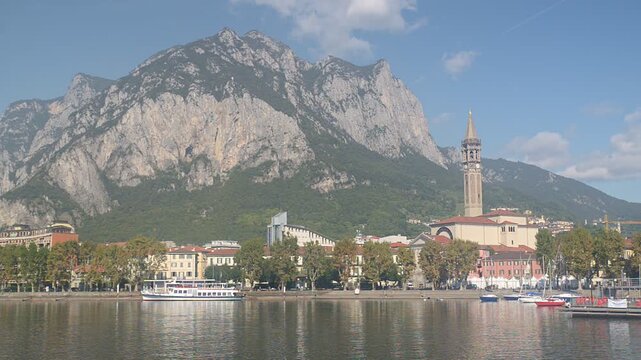 Lecco town on Lake Como with San Nicolo basilica bell tower, boats on the lake and alpine mountains behind the city, sunny early autumn panoramic cityscape, Lombardy Italy travel destination