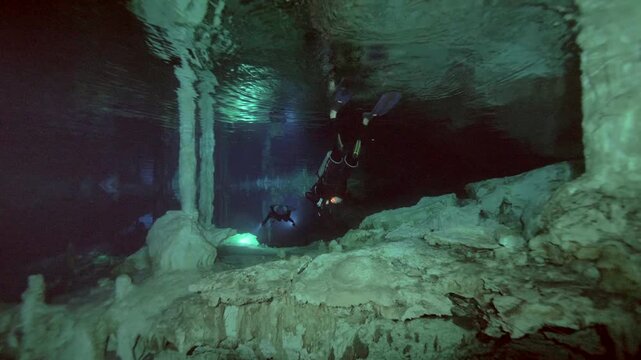Diver and vertical rock column mirrored on water surface creating symmetry in Cenote Dos Ojos, Quintana Roo, Mexico