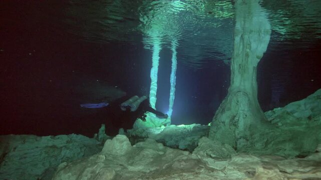Scuba diver shines torch toward tall column highlighting texture and structure in Cenote Dos Ojos, Quintana Roo, Mexico