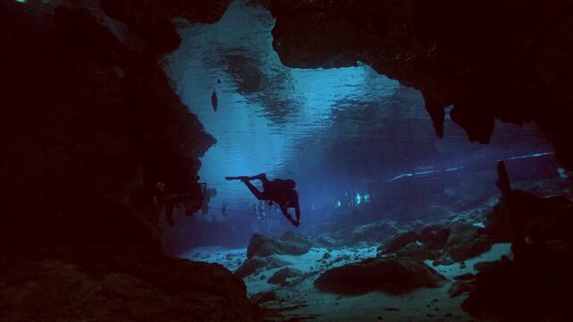 Scuba diver swims toward bright natural light illuminating cave exit in Cenote Dos Ojos, Quintana Roo, Mexico