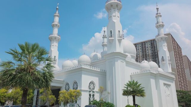 Depok, Indonesia (April 6, 2026): At-Thohir Mosque, An impressive white mosque with tall minarets, lush greenery, and a bright blue sky captures stunning architectural beauty and peaceful ambiance.