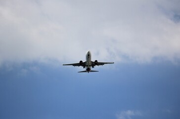 Fototapeta premium Commercial passenger airplane flying overhead against a blue cloudy sky, symbolizing modern air travel, transportation, and global connectivity.
