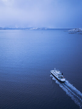 Aerial view of a ferry cutting through the dark blue water, leaving a foamy white trail in its wake, Sommaroy, Troms, Norway.