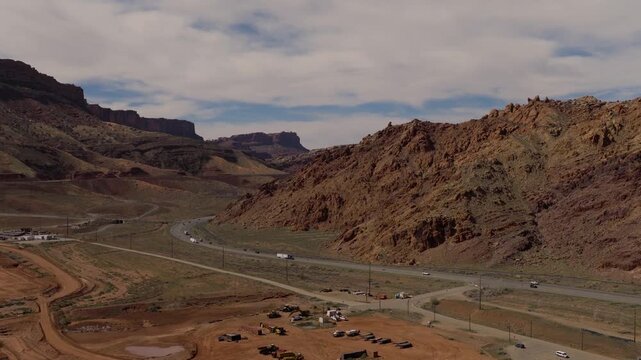 Arches National Park entrance in Moab Utah US 191 with traffic along desert valley below Entrada Sandstone ridge in Colorado Plateau American Southwest red terrain, drone pullback reveal