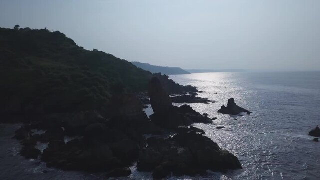 Drone footage glides above rugged rocks along India's Arabian Sea coast, showcasing Nivti Beach and Malvan's scenic Backwaters, Maharashtra shoreline.