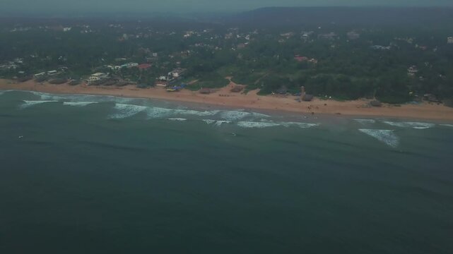 Aerial perspective of Candolim Beach in Goa, India, showing the Arabian Sea meeting the sandy shoreline with residential buildings and lush tropical vegetation inland under overcast skies.