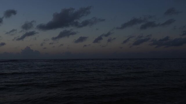 Cinematic wide shot of the ocean at blue hour. Dark waves under a deep indigo sky with scattered altocumulus clouds. Moody, minimalist maritime horizon during late twilight.