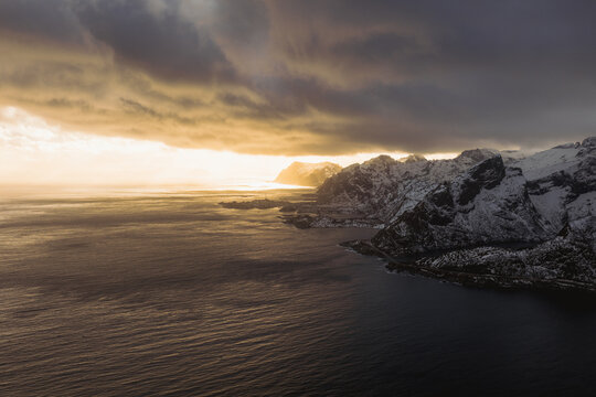 Aerial view of the dramatic coastline meeting the moody waters under an evocative sky, Reinebringen, Nordland, Norway.