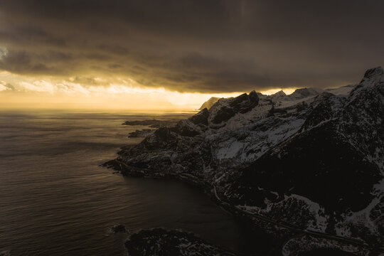 Aerial view of dramatic cliffs meeting the moody sea under a brooding sky, Reinebringen, Nordland, Norway.
